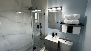 A modern bathroom with a glass shower enclosure, a vanity with a sink and mirror, and a towel rack with neatly folded towels.
