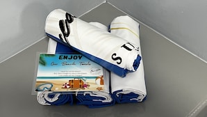 A neatly folded towel with a beach-themed towel bag and a printed towel bag with a beach scene and text.