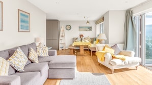 A modern living room with a grey sectional sofa, a white armchair, and a dining area with a wooden table.