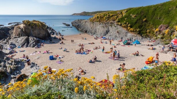 A beach with rocky cliffs, people sunbathing, and tents.