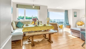 A dining area with a wooden table, chairs, and a view of the sea through large windows.
