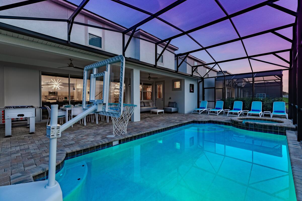 A pool area with a basketball hoop, lounge chairs, and a patio with a table and chairs.