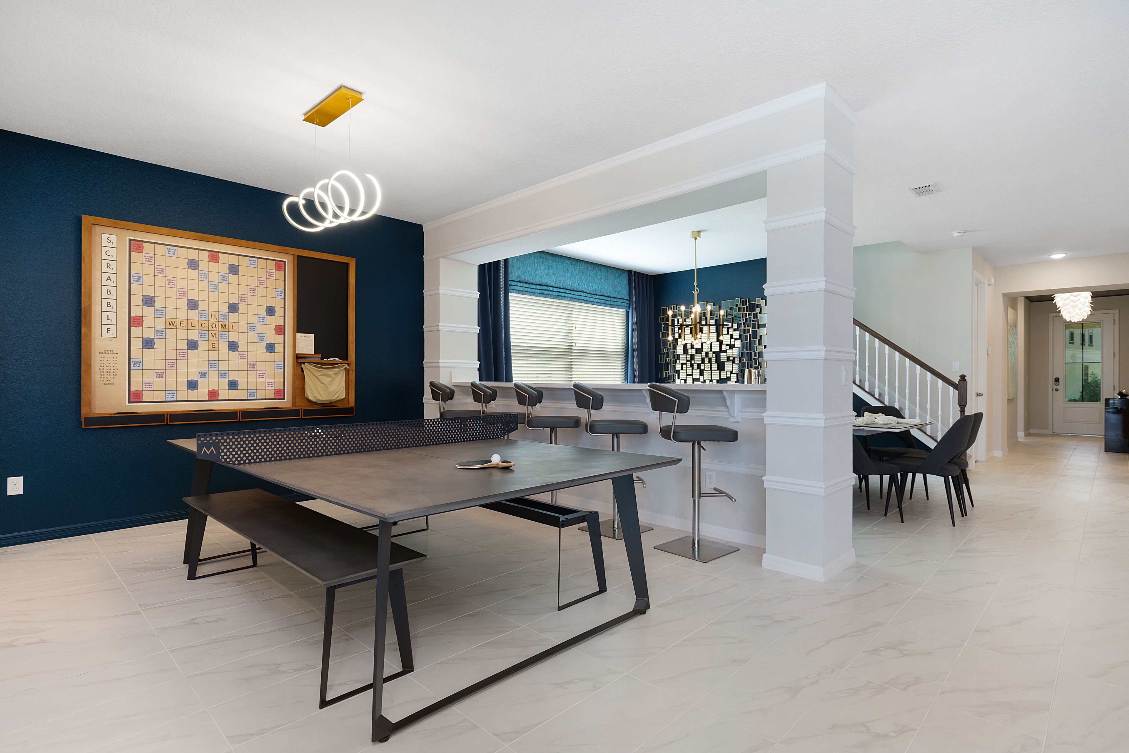 Una sala moderna con un gran tablero de Scrabble, una mesa de centro de madera oscura y una escalera que sube a otro nivel.