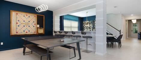 Una sala moderna con un gran tablero de Scrabble, una mesa de centro de madera oscura y una escalera que sube a otro nivel.