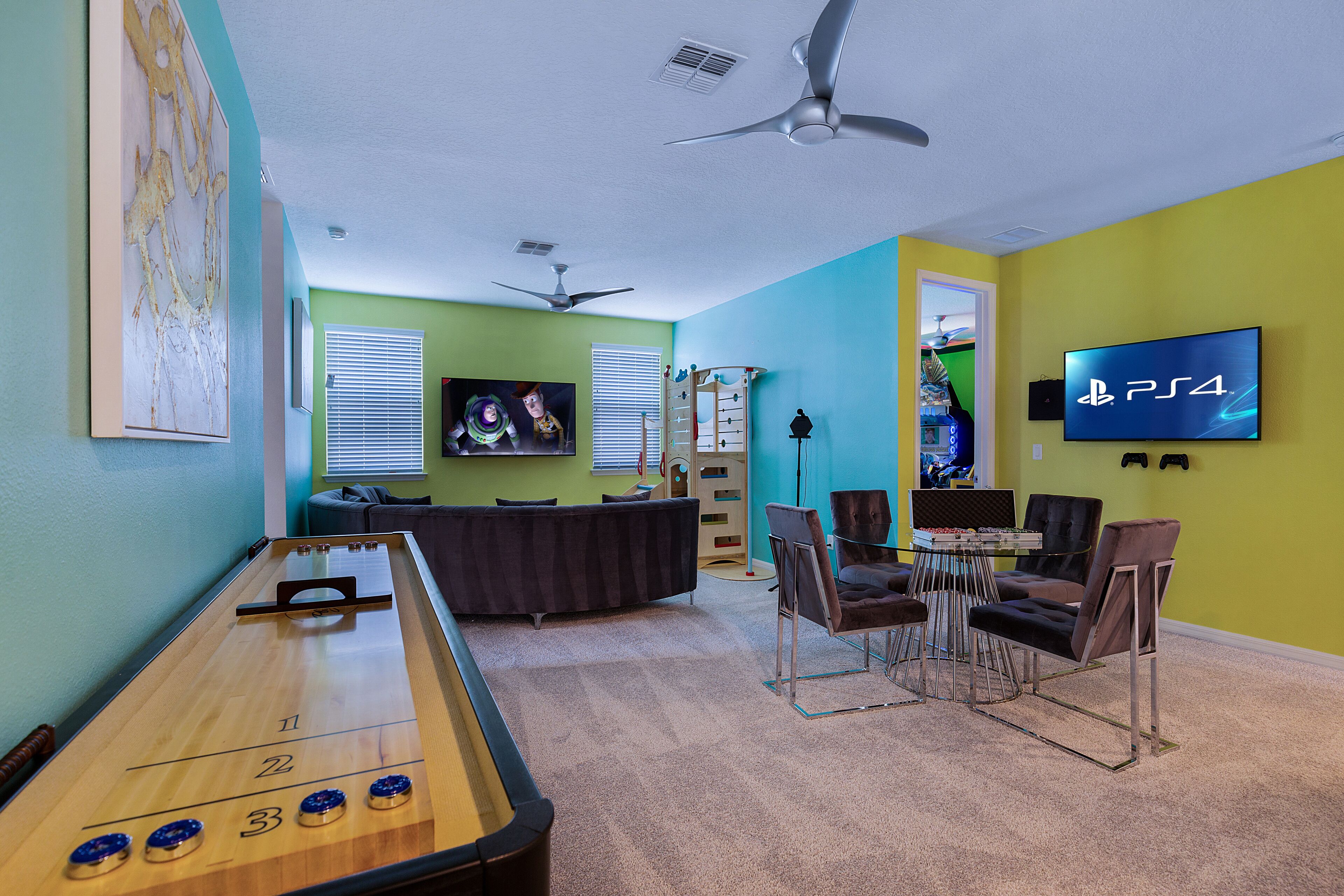 A living room with a shuffleboard table, a PS4 gaming console, and a TV mounted on the wall.