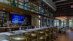 A bar area with a long counter, multiple stools, and a television displaying news. - Villatel at Solara Resort - 8BRs (Kissimmee)