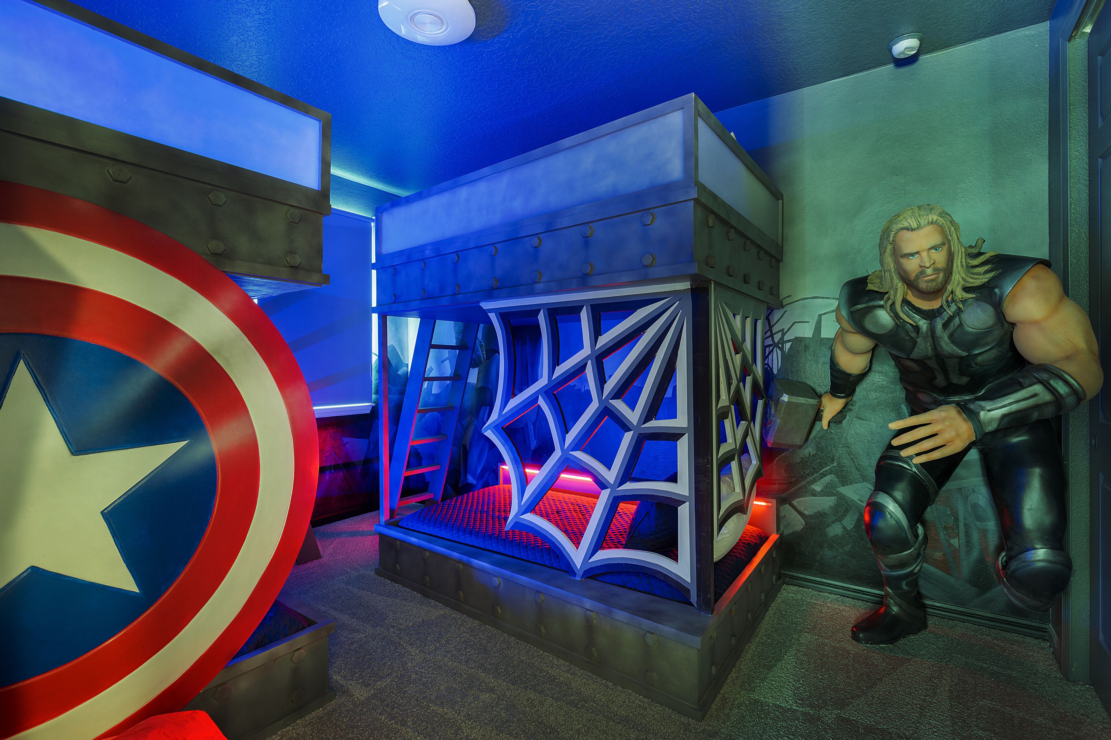 Ein Zimmer mit einem Captain America Schild, einem Bett mit geometrischem Kopfteil und einer Statue einer muskulösen Figur.