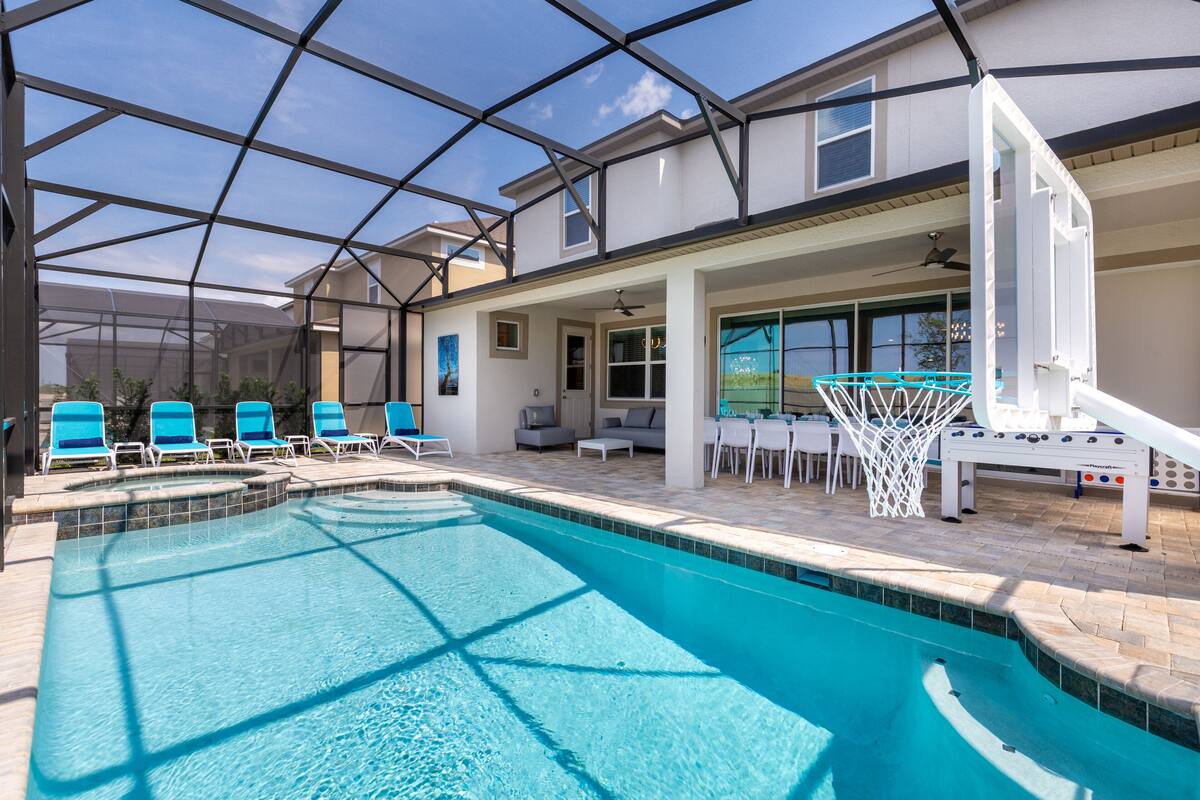 A swimming pool with a glass ceiling, blue chairs, and a basketball hoop.