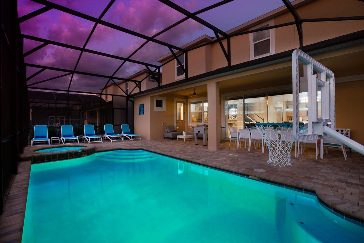 An indoor swimming pool with blue chairs and a basketball hoop.