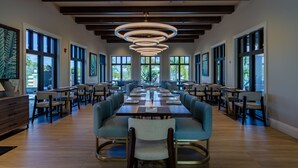 A spacious dining area with long tables and chairs, large windows, and a modern chandelier. - Villatel at Solara Resort - 8BRs (Kissimmee)