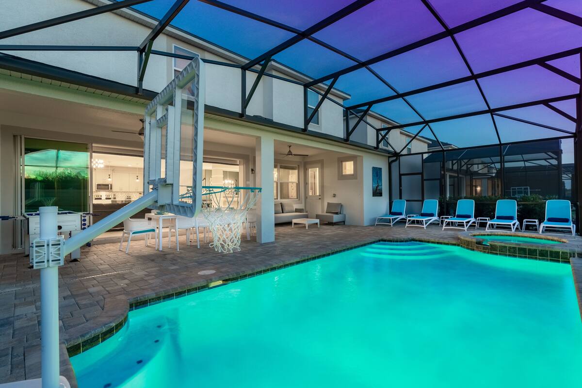 An indoor swimming pool with a glass ceiling, lounge chairs, and a sunroom with a view.