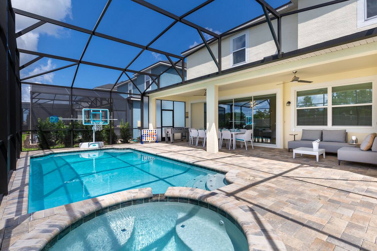 A swimming pool with a glass enclosure, patio furniture, and a covered outdoor area.