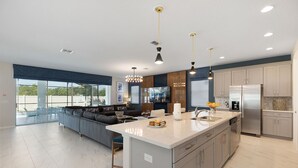 A modern kitchen with a large island, built-in appliances, and a dining area with a sofa and chairs. - Villatel at Solara Resort - 8BRs (Kissimmee)