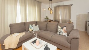 Ein modernes Wohnzimmer mit einer braunen Couch, einem weißen Couchtisch und einer Küchenzeile im Hintergrund.