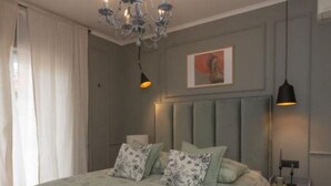 Ein Schlafzimmer mit einem großen Bett, einer Chandelüster, einem Nachttisch und einer Wandlampe.