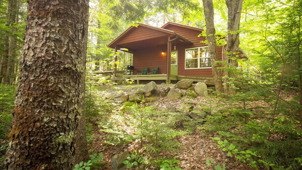 A cabin in a forest with a porch, seating area, and a view of the surrounding trees. - small 2-bedroom chalet in the heart of the wilderness, 5 km from Kejimkujik Park (Maitland Bridge)
