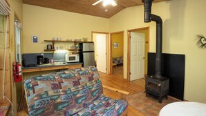 A cozy cabin interior with a kitchenette, a sofa, a dining table, and a wood-burning stove. - small 2-bedroom chalet in the heart of the wilderness, 5 km from Kejimkujik Park (Maitland Bridge)
