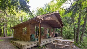 Eine rustikale Holzhütte mit Veranda, zwei grüne Stühle und einem Picknicktisch.
