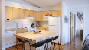 A modern kitchen with wooden cabinets, a central island with bar stools, a microwave, and a refrigerator. - Stunning Mountain Views-Cozy 2 Bedroom (Canmore)