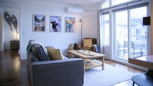 A modern living room with a grey sofa, a wooden coffee table, and a large window with a view of outdoor furniture. - Stunning Mountain Views-Cozy 2 Bedroom (Canmore)