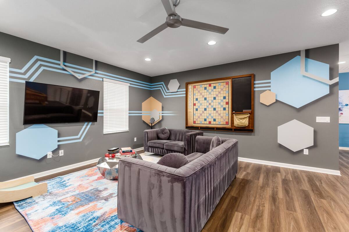 A modern living room with a sectional sofa, a flat-screen TV, and a large window with blinds.