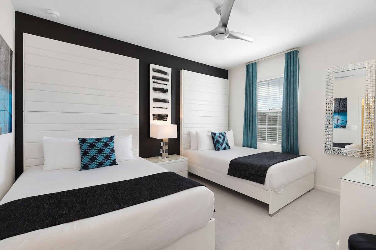 A hotel room with two beds, a ceiling fan, a large mirror, and a window with curtains.