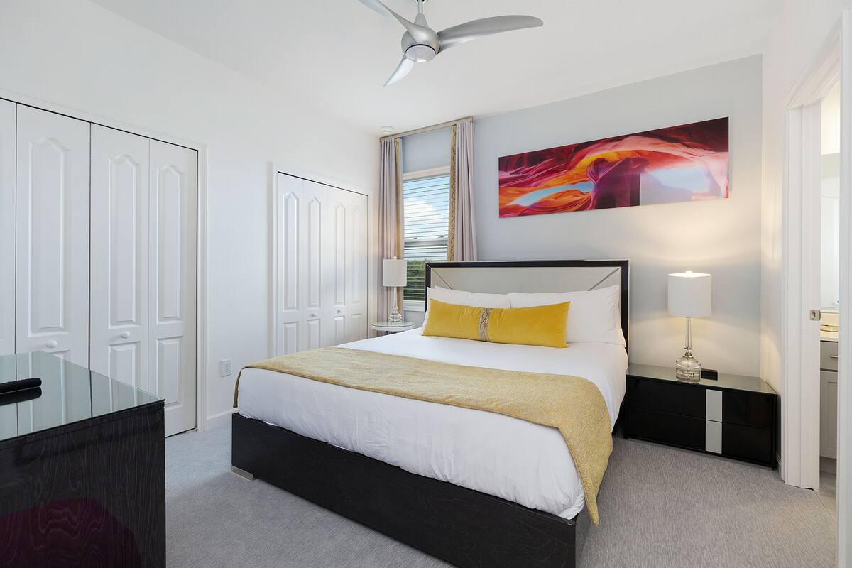 A modern bedroom with a bed, bedside tables, a desk, and a ceiling fan.