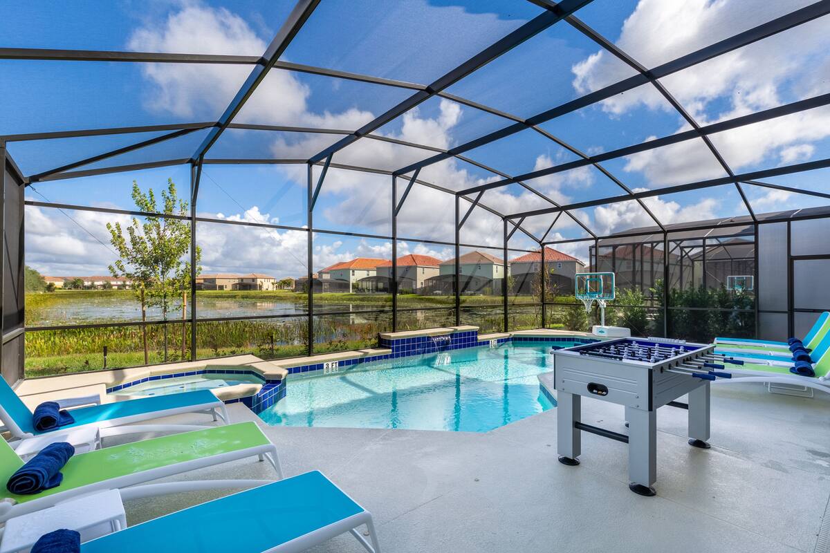A pool area with lounge chairs, a foosball table, and a view of houses through a transparent roof.