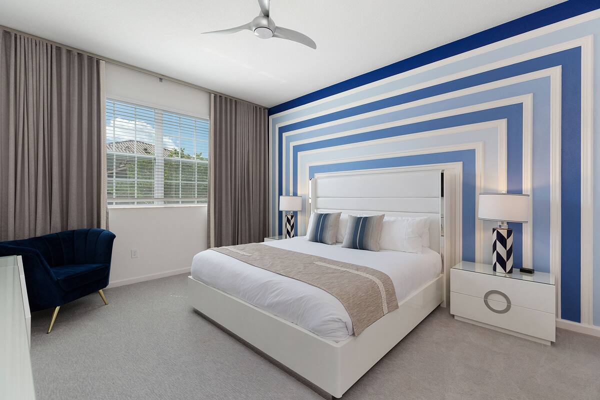 A modern bedroom with a large bed, a nightstand with a lamp, and a ceiling fan.