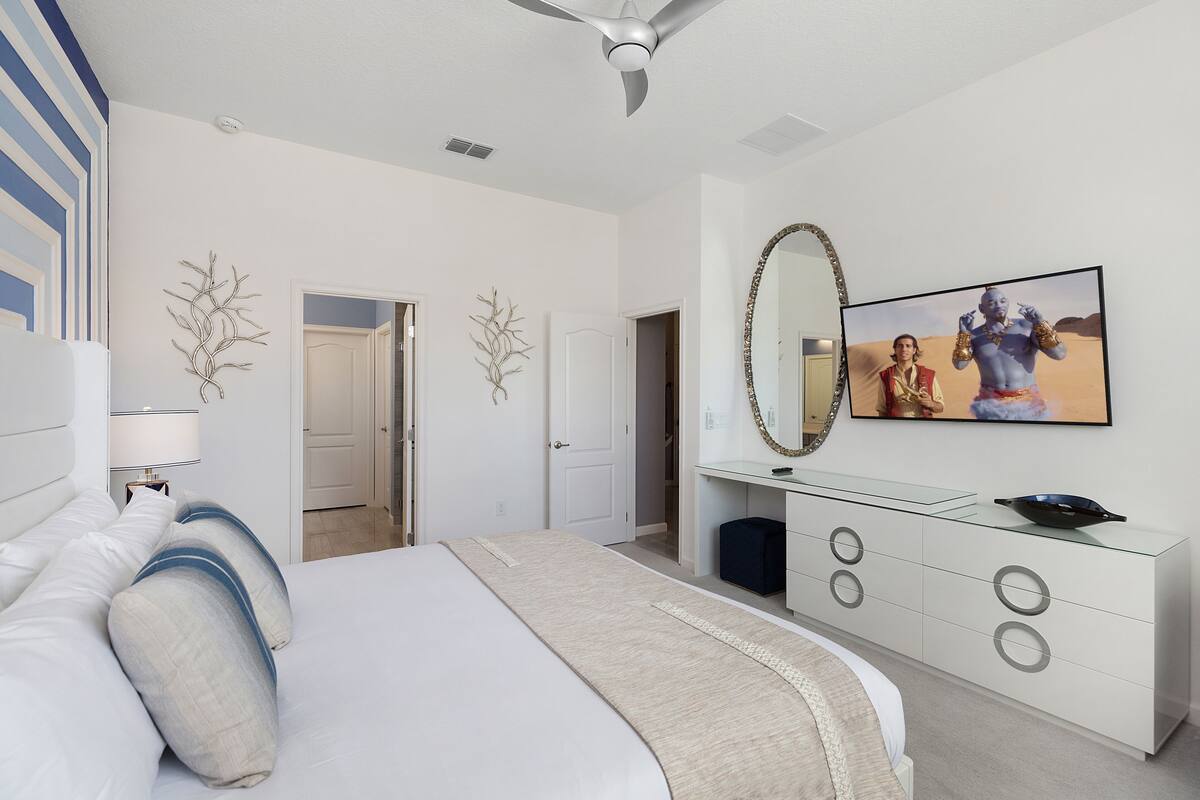 A modern bedroom with a large bed, a glass dresser, and a ceiling fan.