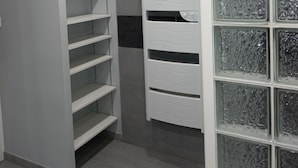 Una habitación con un estante blanco contra una pared gris, un armario blanco con puertas de cristal y un suelo de baldosas grises.