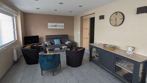 Una sala de estar moderna con un sofá, dos sillones, una mesita de centro y un aparador con puertas de vidrio.