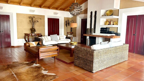 Un salón amplio con un techo alto de madera, un sofá grande tejido, un banco de cuero y una alfombra de piel en el suelo.