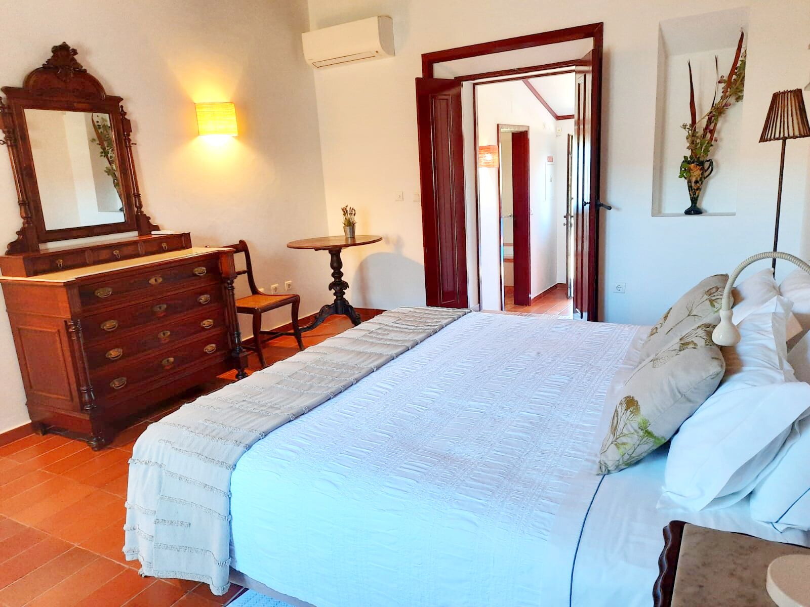 Une chambre à coucher comprenant un lit, une commode, un miroir, une lampe et une petite table sur laquelle est posée une plante.
