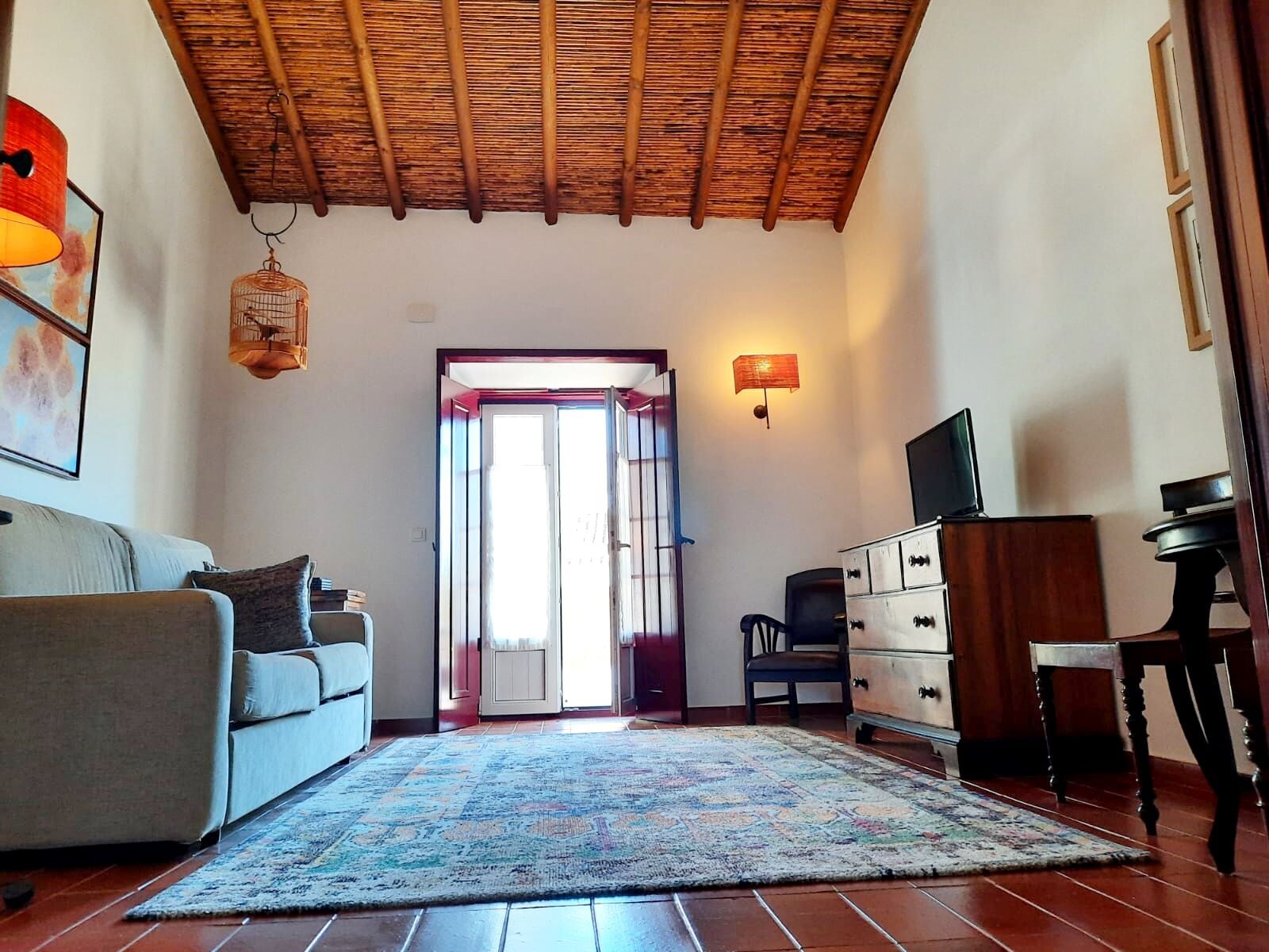 Un salon comprenant un canapé, un tapis à motifs, un plafond en bois, un téléviseur et un meuble.
