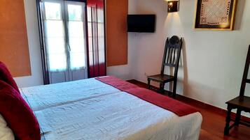 A bedroom with a bed, a chair, a television, and a window with curtains.