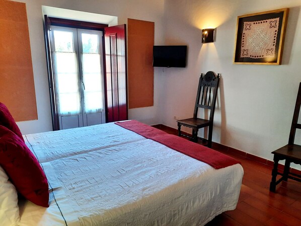 A bedroom with a bed, a chair, a television, and a window with curtains.