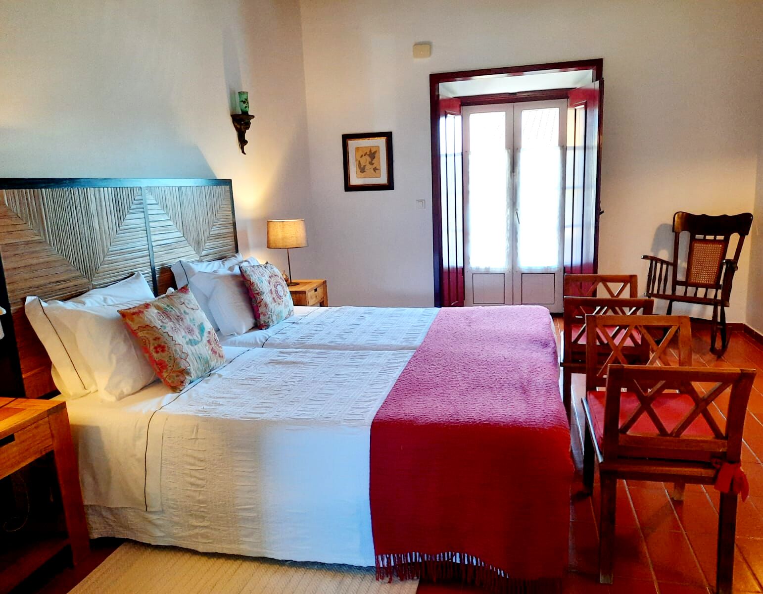 Un letto matrimoniale con testiera, comodini, una lampada, un quadro incorniciato e una sedia.