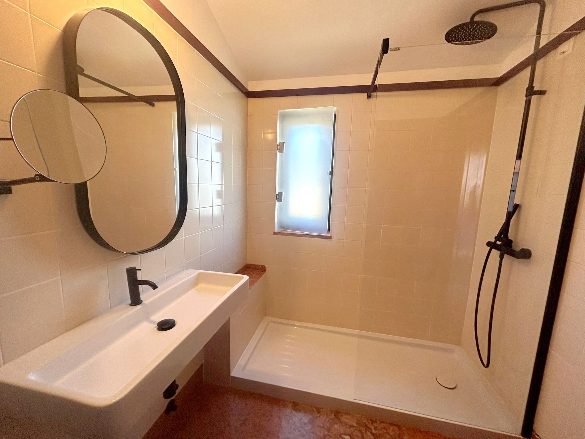 A bathroom with a white sink, a mirror, a shower with a handheld showerhead, and a window.