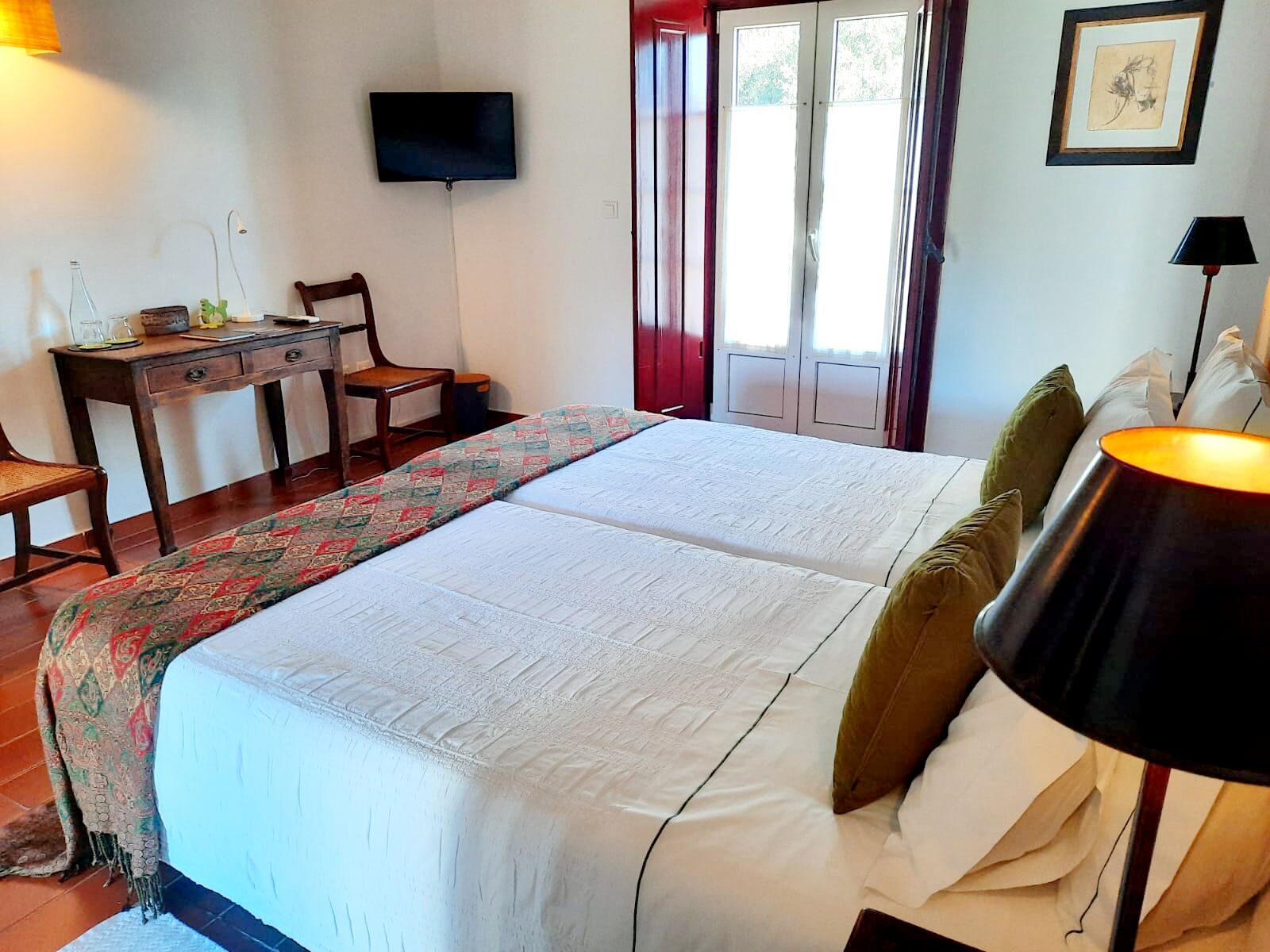 Habitación de hotel con cama, escritorio, silla, televisor y ventana con cortinas.