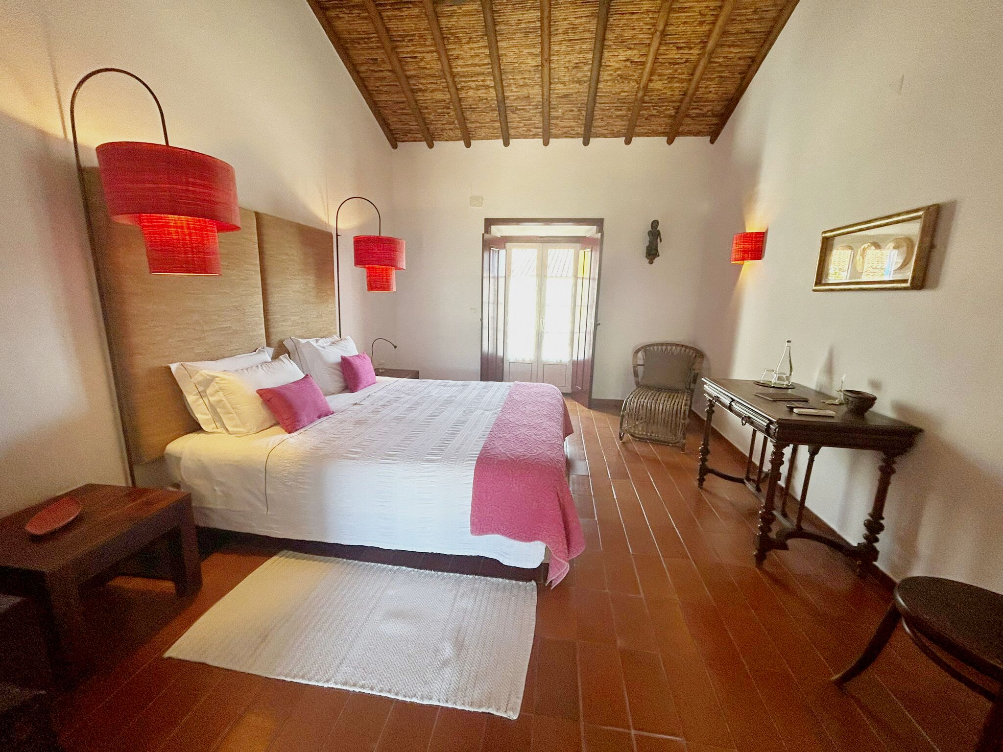A bedroom with a bed, bedside tables, a chair, a table, and a door.