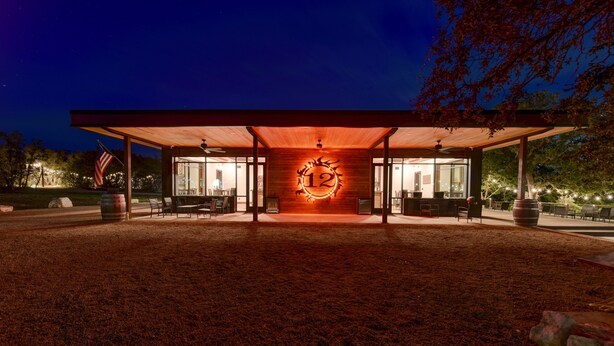 A modern building with a large illuminated number '12' on the facade, surrounded by outdoor seating and a flag.