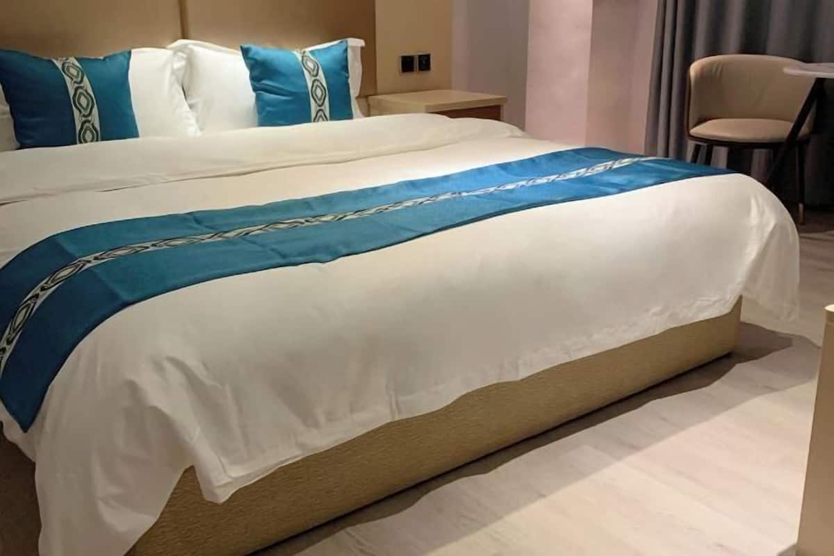 A neatly made bed with a blue and white bedspread, a wooden headboard, and a small bedside table with a lamp.