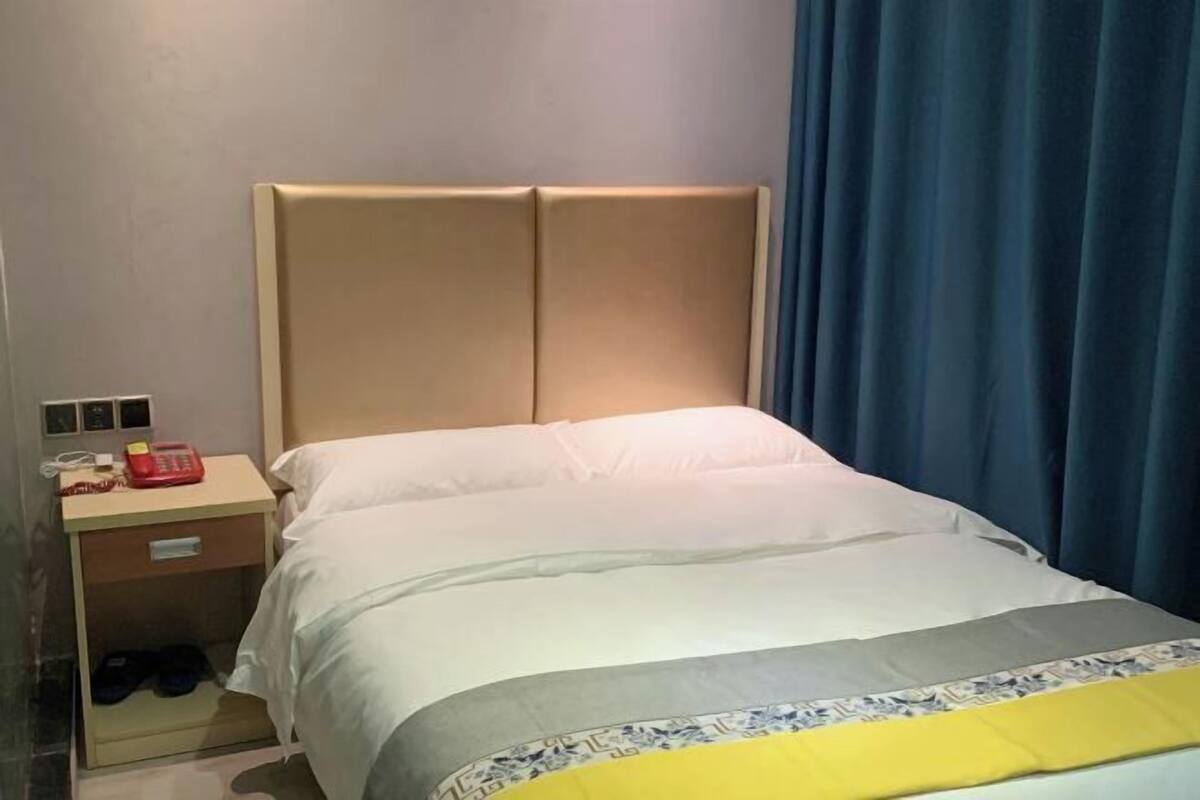 A hotel room with a bed, a nightstand, a telephone, and a pair of slippers.