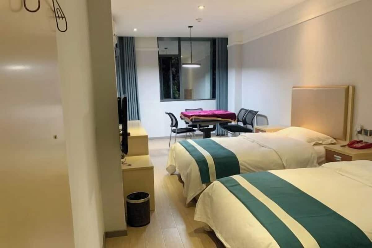 A hotel room with two beds, a desk, a chair, a TV, and a window with curtains.