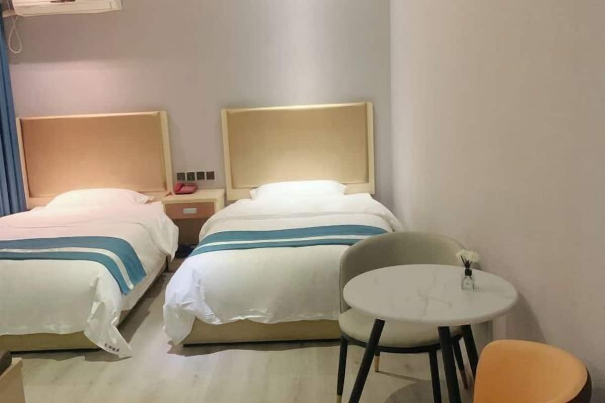 A hotel room with two beds, a small round table, and a chair.