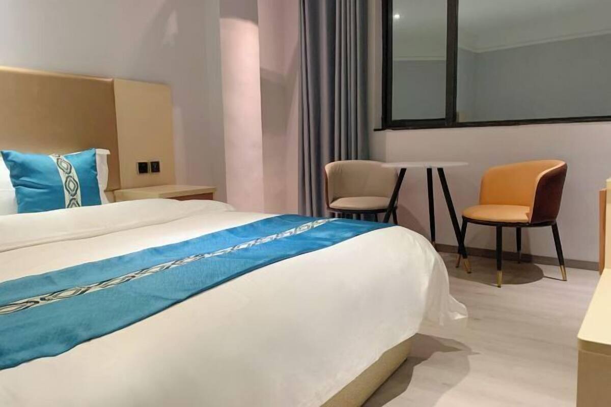A hotel room with a large bed, a small table, two chairs, and a window with curtains.