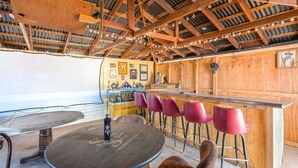 Un intérieur rustique en bois, avec un coin bar, des tabourets de bar rouges et un plafond en bois avec des poutres apparentes.
