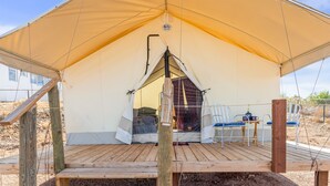 A tent with a wooden deck, a table with chairs, and a view of the desert landscape.