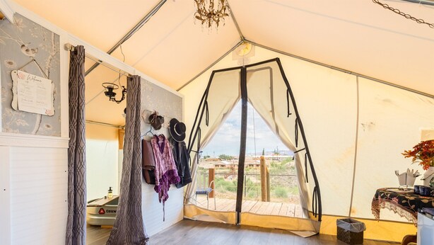 A tented room with a wooden floor, a swing bed, a hanging light fixture, and a view of the outdoors.